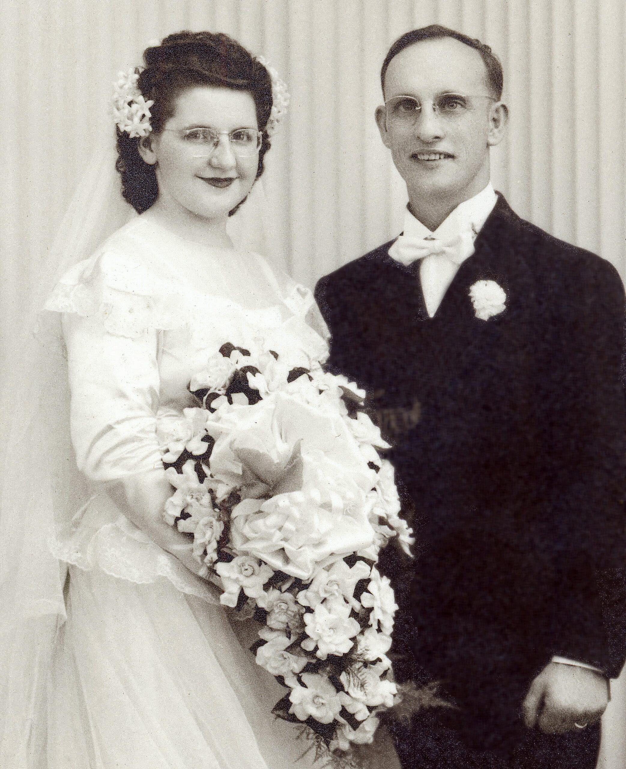 1940s bride wearing wax hair flower veil and vintage wave hairstyle standing next to groom in studio